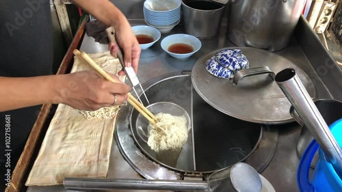 Hands of an adult man boiling and preparing pork noodles or Wan Tha Mie, a typical Chinese food from Riau, in the kitchen of a restaurant.