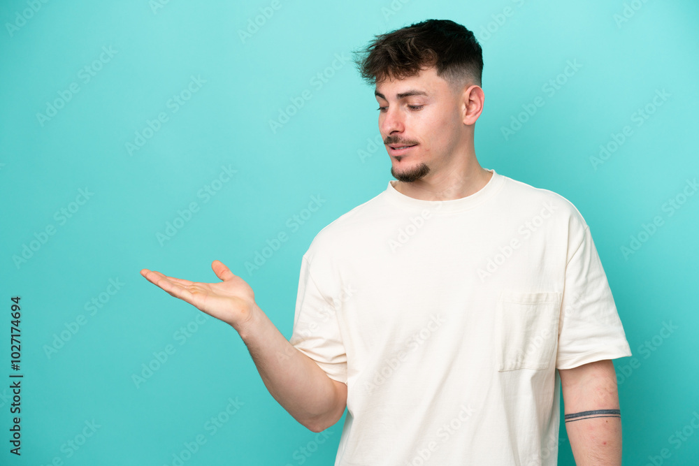 Young caucasian handsome man isolated on blue background holding copyspace with doubts Young caucasian handsome man isolated on blue background holding copyspace with doubts