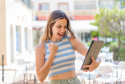 Free Download Young pretty woman holding a tablet at outdoors celebrating a victory - GFXLoad