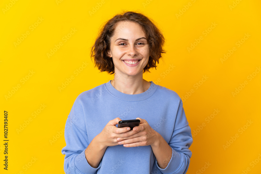 Young English woman isolated on pink background looking at the camera and smiling while using the mobile Young English woman isolated on pink background looking at the camera and smiling while using the mobile