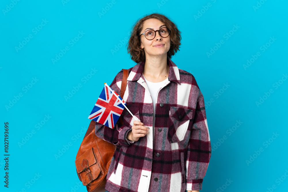 Young English woman holding an United Kingdom flag isolated on blue background and looking up Young English woman holding an United Kingdom flag isolated on blue background and looking up