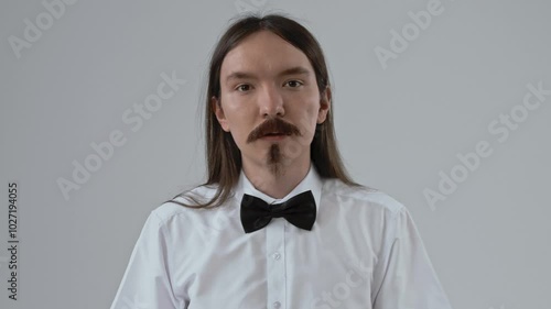 Guy with long hair puts on a false moustache and beard and poses for the camera. White background 