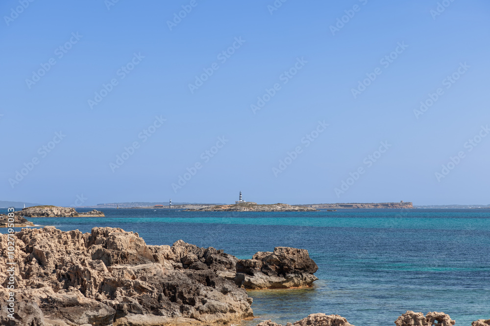 View from Ibiza rocky coastline towards the maritime islands of Formentera, featuring clear blue waters and distant lighthouses on the horizon View from Ibiza rocky coastline towards the maritime islands of Formentera, featuring clear blue waters and distant lighthouses on the horizon