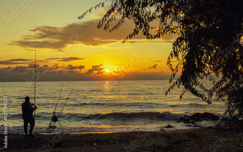 A serene scene of a person fishing by a calm Aegean sea at sunset, capturing a moment of peace and reflection with the golden glow of the setting sun over calm waters.