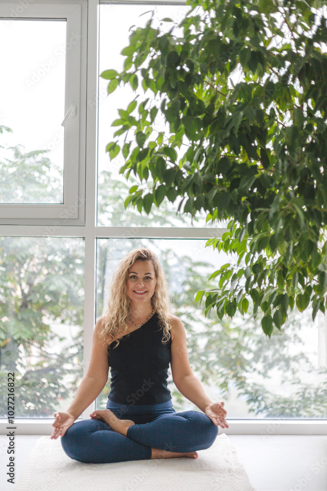 Woman yoga meditation sitting in lotus position near panorama window with houseplant at home Woman yoga meditation sitting in lotus position near panorama window with houseplant at home