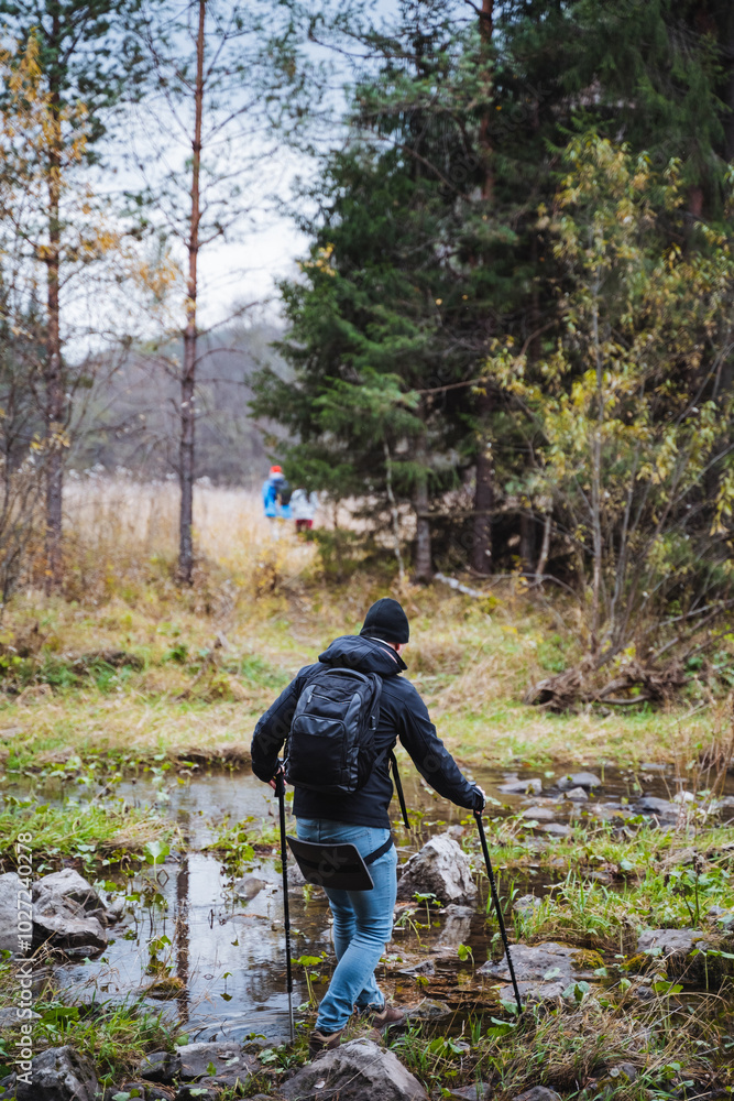 A hiker is carefully crossing a refreshing stream in a breathtakingly beautiful forest landscape, fully surrounded by natures wonders A hiker is carefully crossing a refreshing stream in a breathtakingly beautiful forest landscape, fully surrounded by natures wonders
