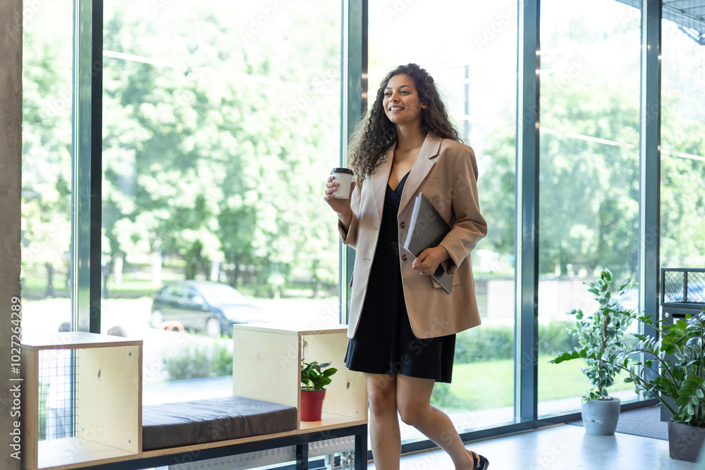Businesswoman walking along the office corridor with documents and paper cup. Businesswoman walking along the office corridor with documents and paper cup.