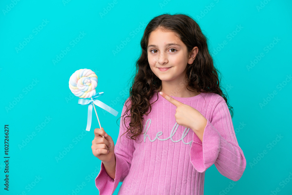 Little caucasian girl holding a lollipop isolated on blue background and pointing it Little caucasian girl holding a lollipop isolated on blue background and pointing it