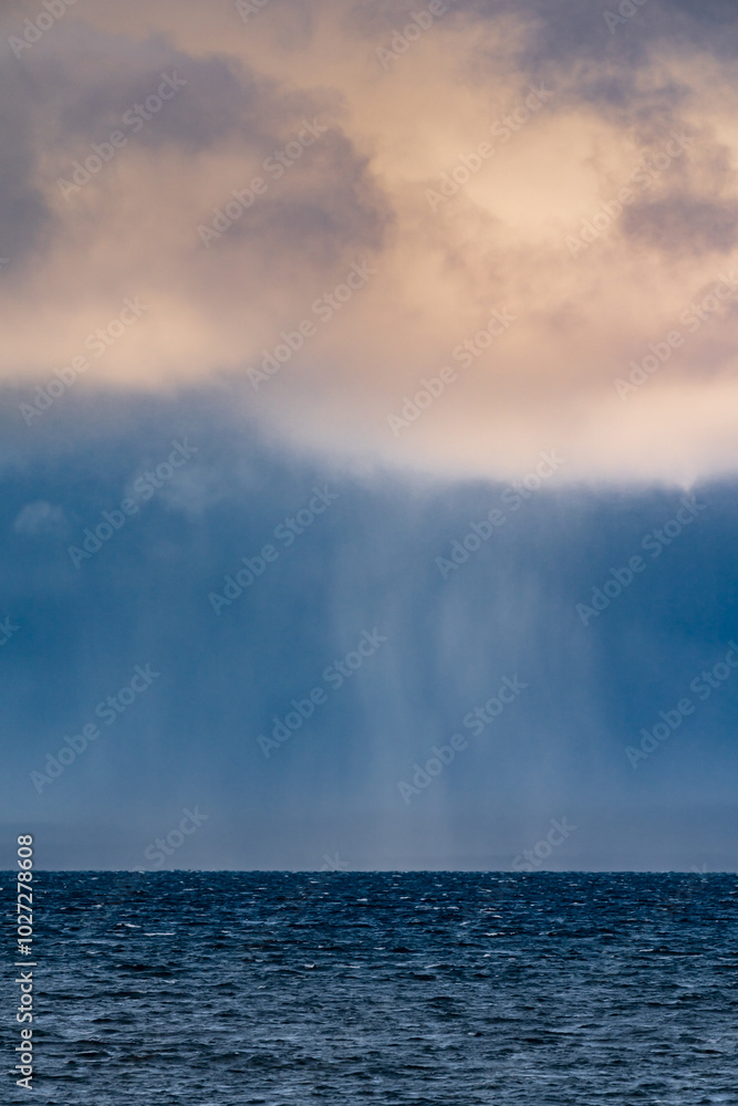 Distant view of rain falling from clouds in a dark sky over a distant coastline Distant view of rain falling from clouds in a dark sky over a distant coastline