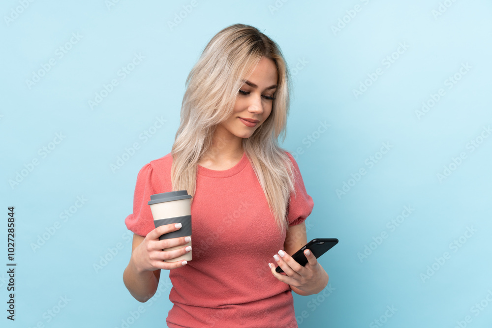 Teenager girl over isolated blue background holding coffee to take away and a mobile Teenager girl over isolated blue background holding coffee to take away and a mobile