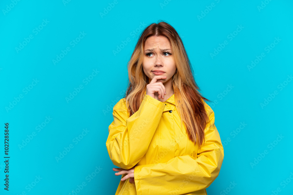 Teenager girl wearing a rainproof coat over isolated blue background having doubts and thinking Teenager girl wearing a rainproof coat over isolated blue background having doubts and thinking