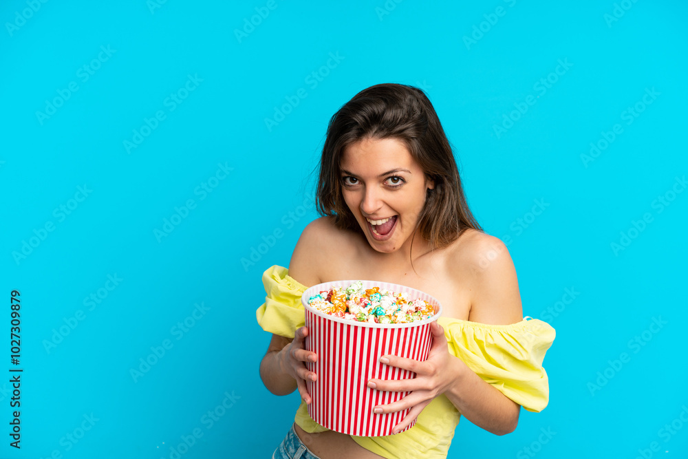 Young caucasian woman isolated on blue background holding a big bucket of popcorns Young caucasian woman isolated on blue background holding a big bucket of popcorns