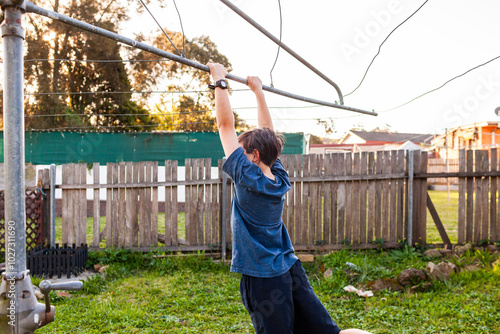 First Nations Australian kid swinging on hills hoist rotary clothesline in Aussie backyard photo