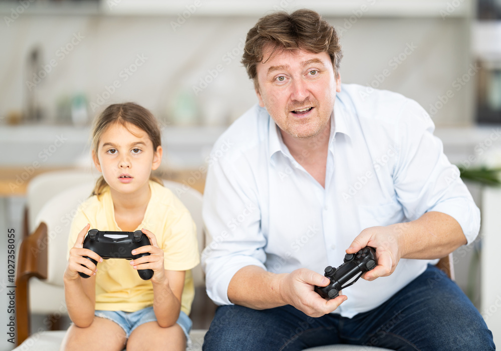 Fototapeta premium Family, gaming and entertainment concept - happy father and little daughter with gamepads playing video game