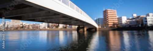 A partially blurred cityscape showing a modern bridge spanning a calm river, capturing themes of urbanization, architecture, and the relationship between cities and nature. #1027371811