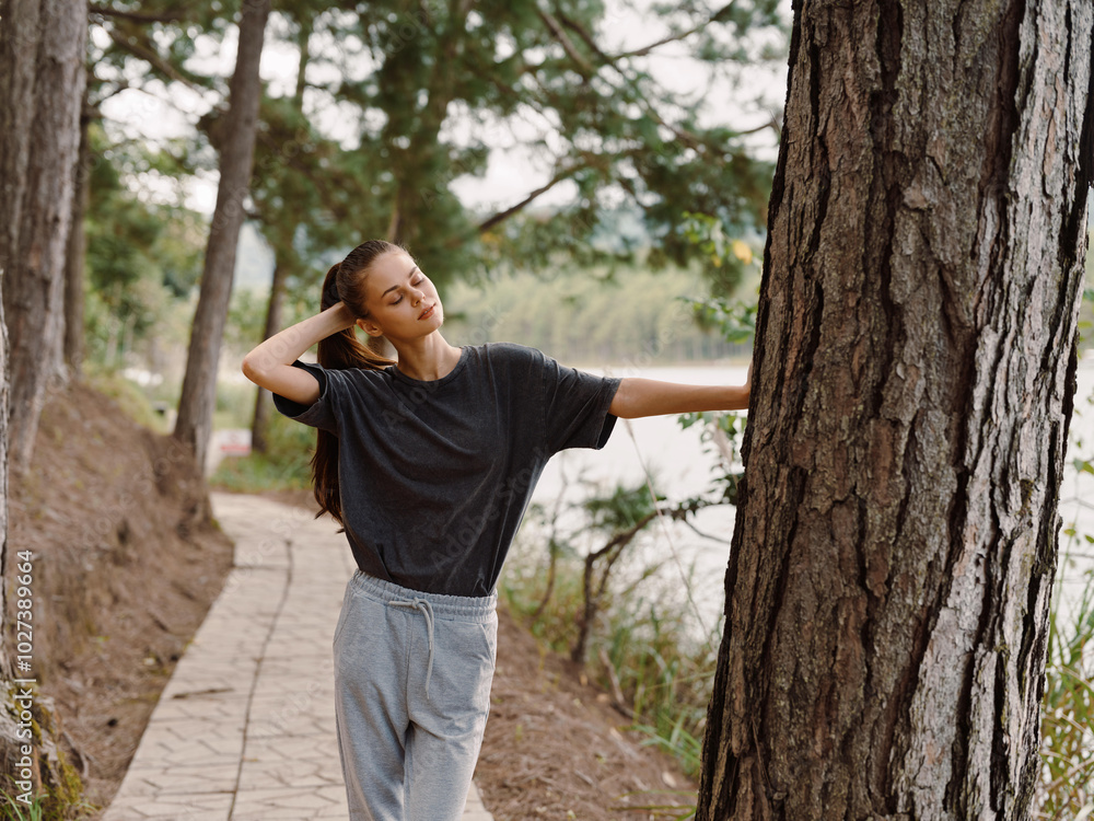 Relaxed young woman leaning against a tree by a serene lakeside path, enjoying nature and the fresh air Representing peace and tranquility in the outdoors Relaxed young woman leaning against a tree by a serene lakeside path, enjoying nature and the fresh air Representing peace and tranquility in the outdoors