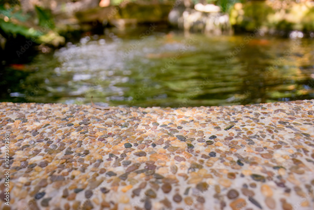 Fototapeta premium Pebble Stone Texture with Blurred Pond in Background.