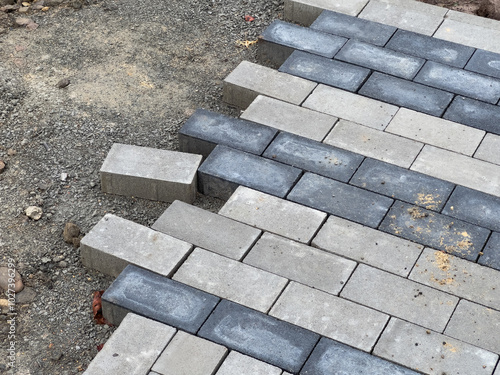 Workers are carefully laying down paving stones on a gravel foundation, progressing through the pavement repair project in this residential neighborhood photo