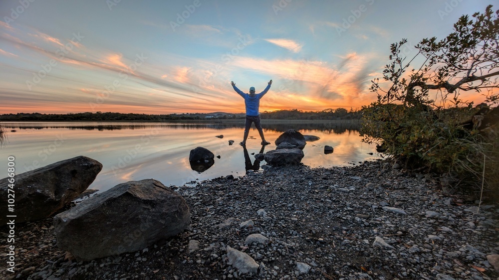 Beautiful orange sunset lakeside landscape scenery, man reflected in water at Ballyquirke lough, Galway, Ireland, nature background