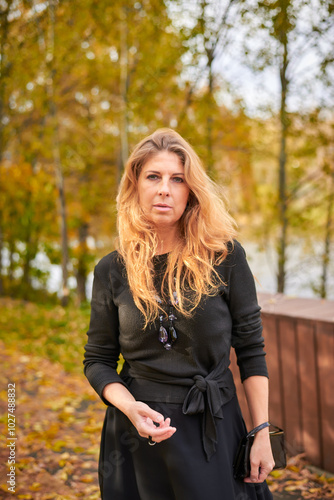 Beautiful woman in black dress and necklace walking in autumn forest. Relaxation concept