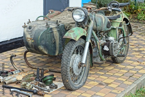 one old green iron retro dirty powerful heavy with sidecar historical military army broken with glass electric headlight and wheels stands on concrete road near white wall daytime outdoors