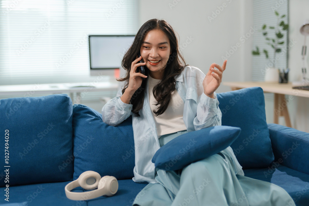 Young woman is having a pleasant phone conversation while relaxing on a comfortable sofa in a bright and airy living room Young woman is having a pleasant phone conversation while relaxing on a comfortable sofa in a bright and airy living room