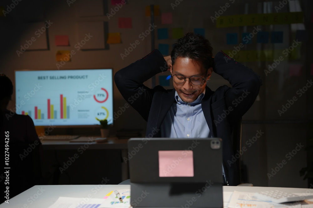 Asian businessman is relaxing stretching his arms at his desk while working late at night in the office Asian businessman is relaxing stretching his arms at his desk while working late at night in the office