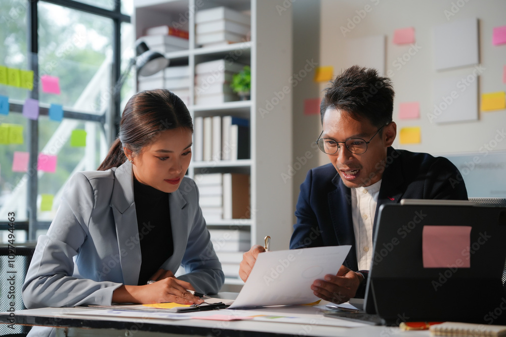 Two young professionals are working together, reviewing documents and talking in their office Two young professionals are working together, reviewing documents and talking in their office