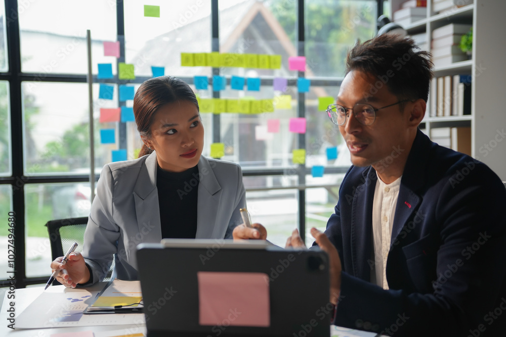 Two business people having a meeting discussing a new project using sticky notes on a glass wall in the office Two business people having a meeting discussing a new project using sticky notes on a glass wall in the office