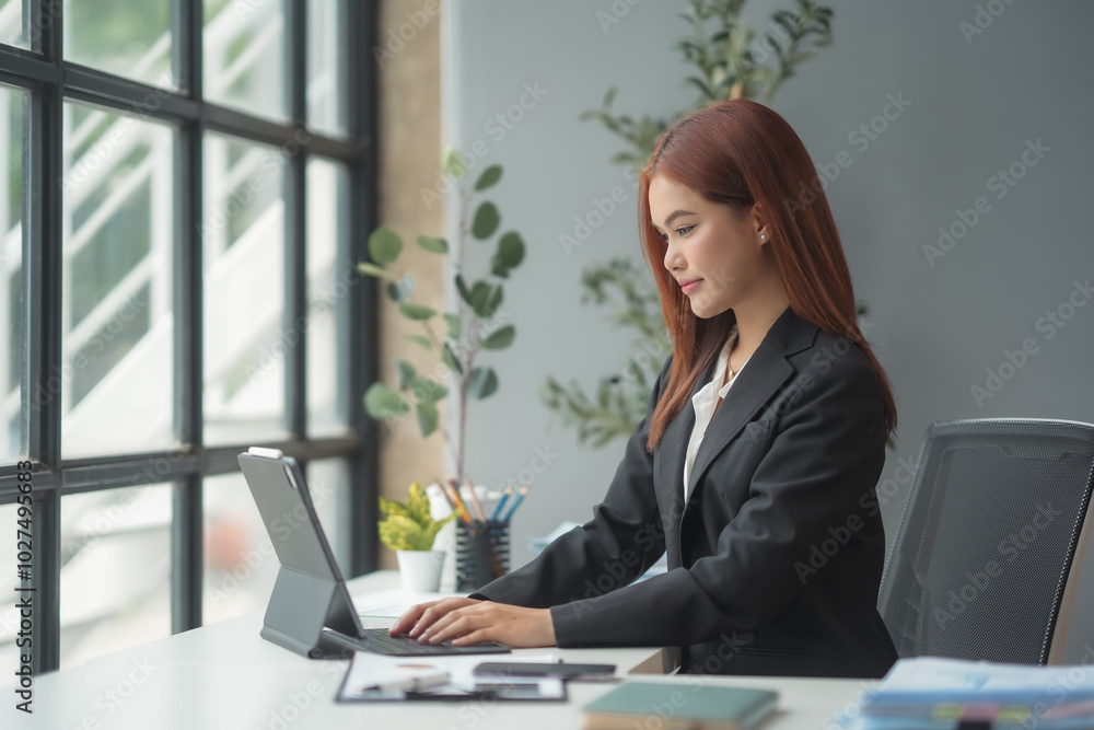 Smiling businesswoman in a bright office, working on a tablet, exuding confidence and focus. The natural light highlights her modern workspace, showcasing her leadership in a professional suit Smiling businesswoman in a bright office, working on a tablet, exuding confidence and focus. The natural light highlights her modern workspace, showcasing her leadership in a professional suit