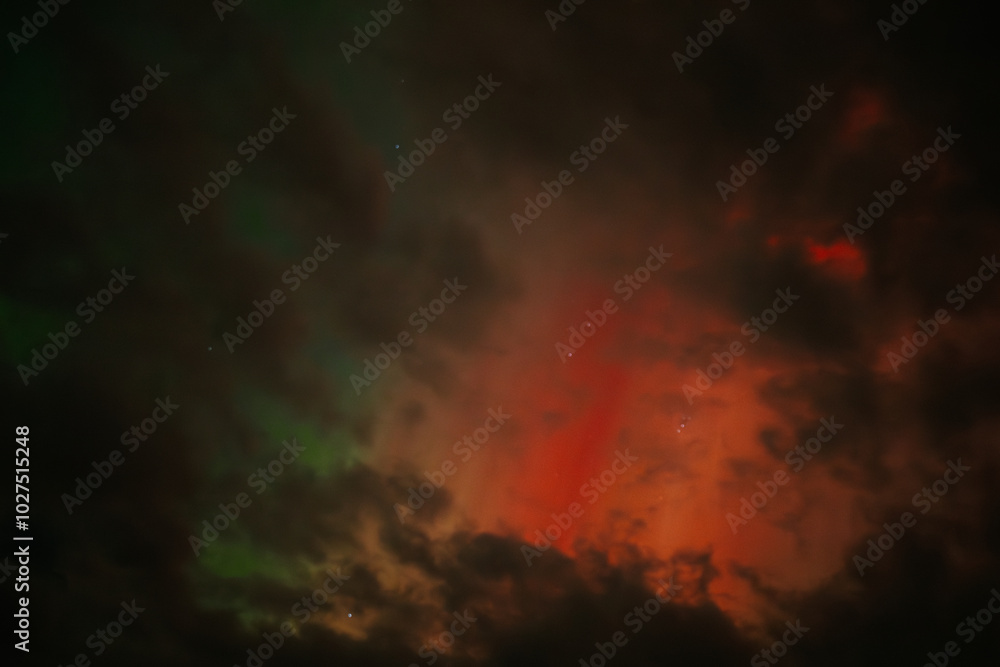 Fototapeta premium A captivating scene of the Aurora Borealis with vibrant red and orange hues illuminating the night sky. Dark clouds add drama, while subtle green light emerges through the atmosphere