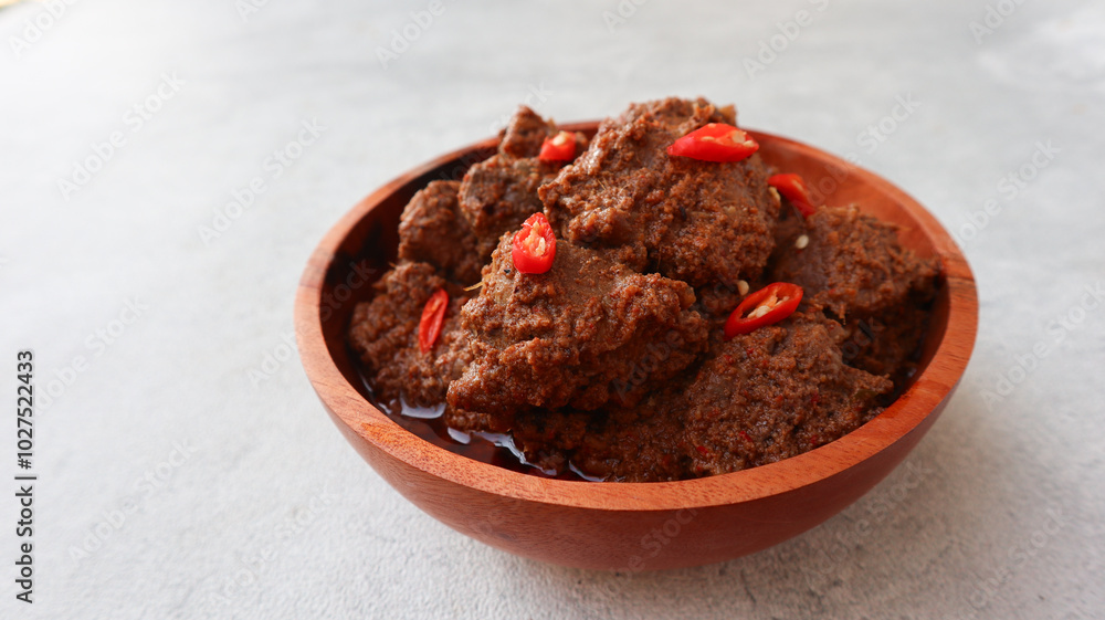 Rendang daging. Spicy beef stew from Padang, Indonesia. The dish is arranged among the spices and herbs used in the recipe. isolated on grey background Rendang daging. Spicy beef stew from Padang, Indonesia. The dish is arranged among the spices and herbs used in the recipe. isolated on grey background