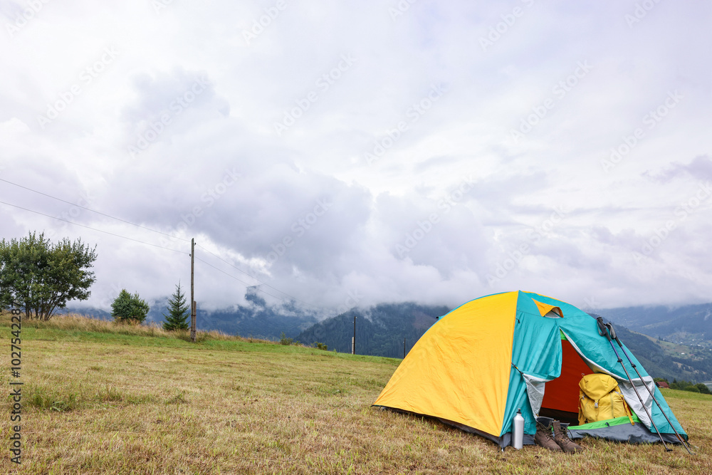 Camping tent and tourist stuff on grass in mountains, space for text Camping tent and tourist stuff on grass in mountains, space for text