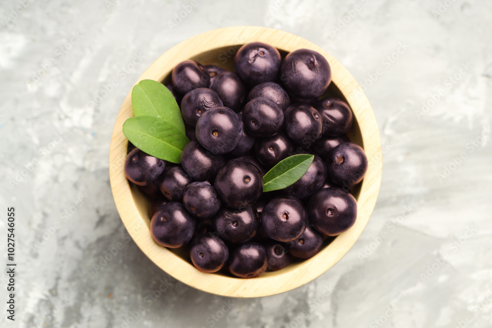 Ripe acai berries and leaves in bowl on grey textured table, top view Ripe acai berries and leaves in bowl on grey textured table, top view