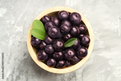 Ripe acai berries and leaves in bowl on grey textured table, top view photo