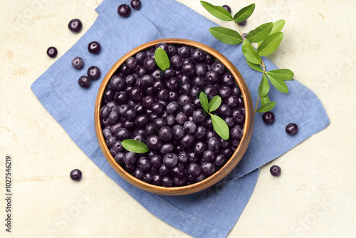 Ripe acai berries and leaves in bowl on light table, flat lay photo