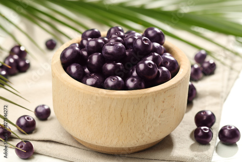 Ripe acai berries in bowl on light table, closeup photo