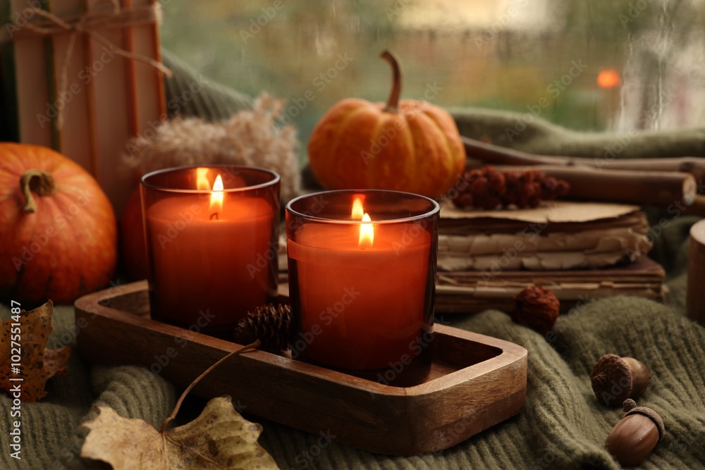 Burning candles, books and autumn decor on green sweater near window Burning candles, books and autumn decor on green sweater near window