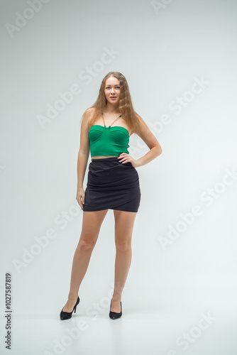 Woman in green top and black skirt posing in front of camera. She has long hair, she is standing on white background. Beautiful sexy body. Fitness and healthy eating concept.