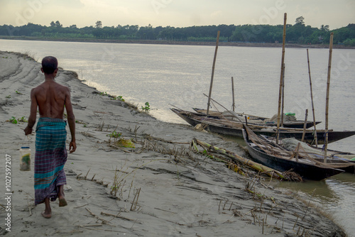 Riverside people of Bangladesh. A fisherman is walking along the river bank. The river flows along the side.