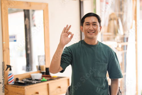 A man is confidently giving an ok sign while sitting in a barber shop, showcasing his satisfaction with the service he is receiving