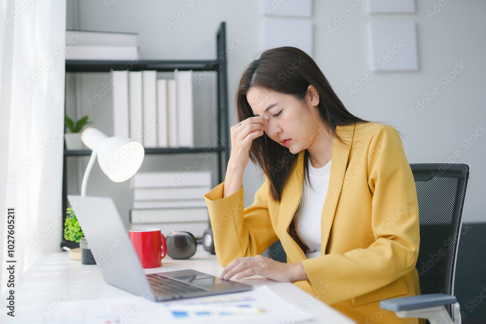 Young businesswoman is feeling stressed and having a headache while working on a laptop at her desk in a modern office Young businesswoman is feeling stressed and having a headache while working on a laptop at her desk in a modern office