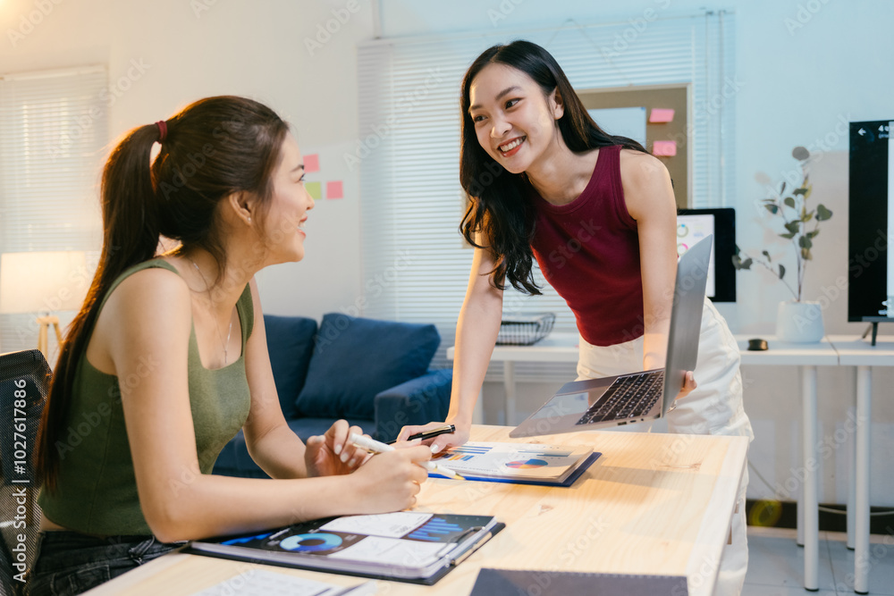Two asian businesswomen are having a discussion over a laptop in their modern startup office. They are both smiling and looking very happy with their work Two asian businesswomen are having a discussion over a laptop in their modern startup office. They are both smiling and looking very happy with their work