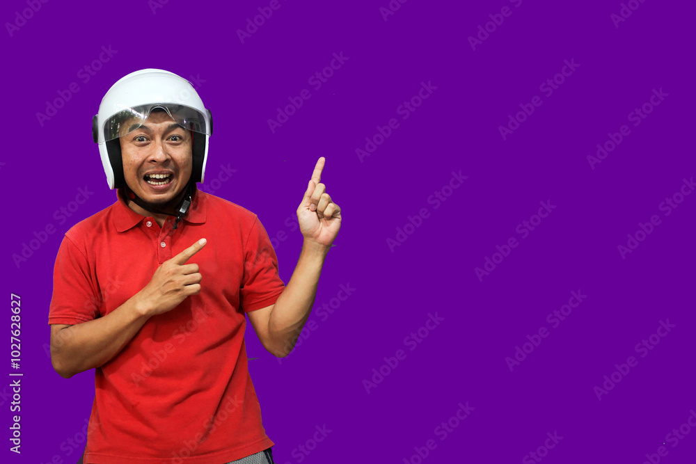 Young Asian driver man wearing helmet looking up while raising both hands and pointing upwards with happy expression
Young Asian driver man wearing helmet looking up while raising both hands and pointing upwards with happy expression