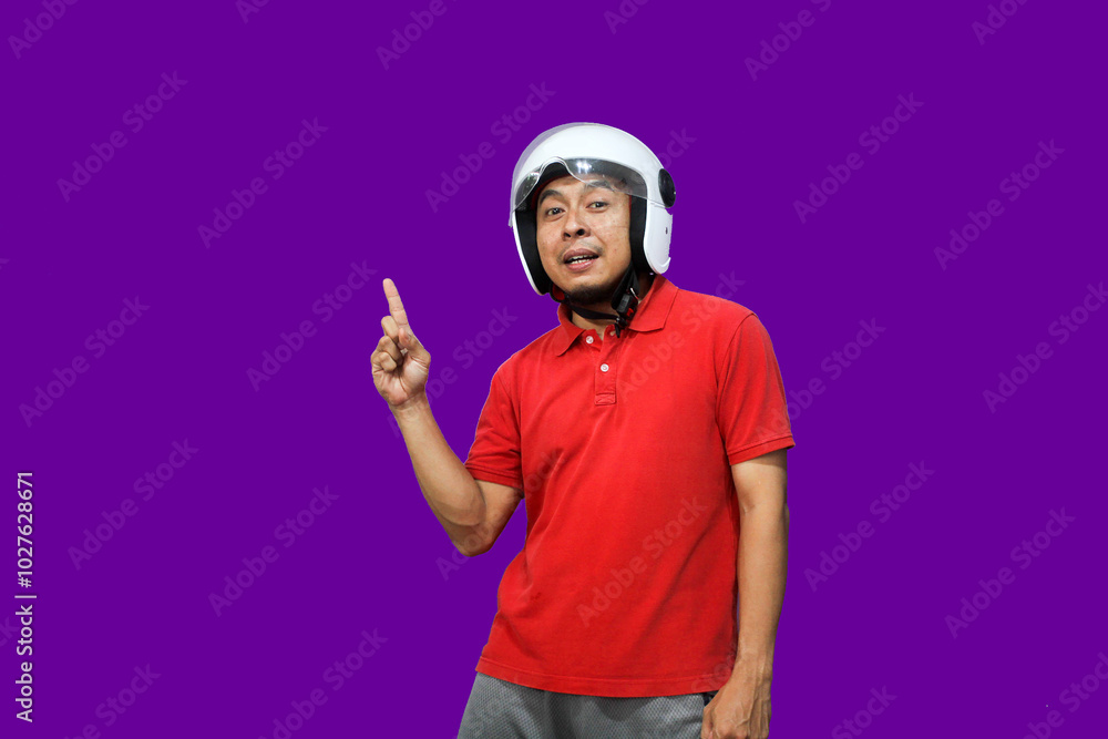 Young Asian driver man wearing helmet looking up while raising one hand and pointing upwards with happy expression
Young Asian driver man wearing helmet looking up while raising one hand and pointing upwards with happy expression