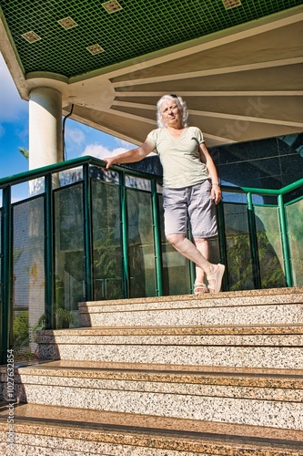 An elderly woman stands on the stairs of a modern building and looks at the camera.