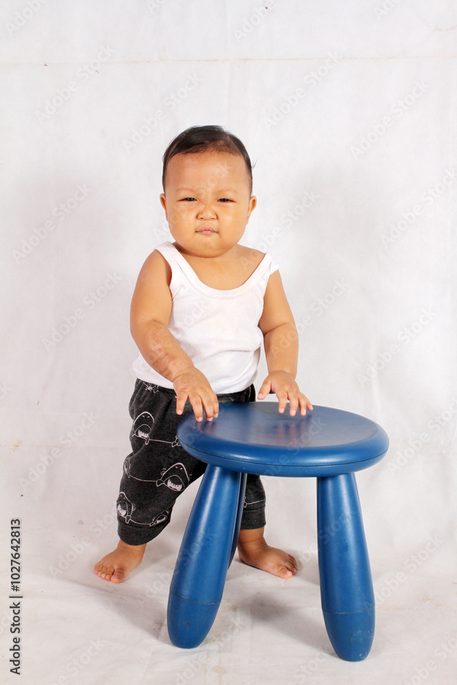 Adorable one year old Asian baby boy is sitting on a plastic chair wearing an undershirt Adorable one year old Asian baby boy is sitting on a plastic chair wearing an undershirt