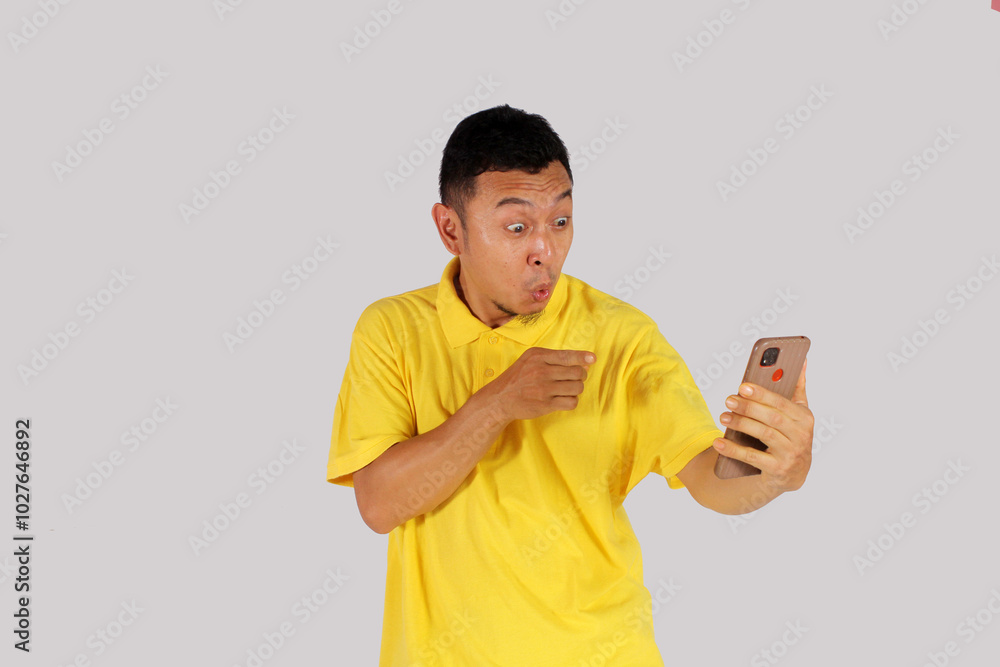 A man shows a happy expression by holding a cellphone while pointing at it
A man shows a happy expression by holding a cellphone while pointing at it