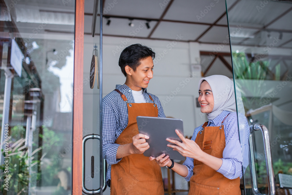 veiled woman and male waiter using a tablet together standing in front of a coffee shop veiled woman and male waiter using a tablet together standing in front of a coffee shop