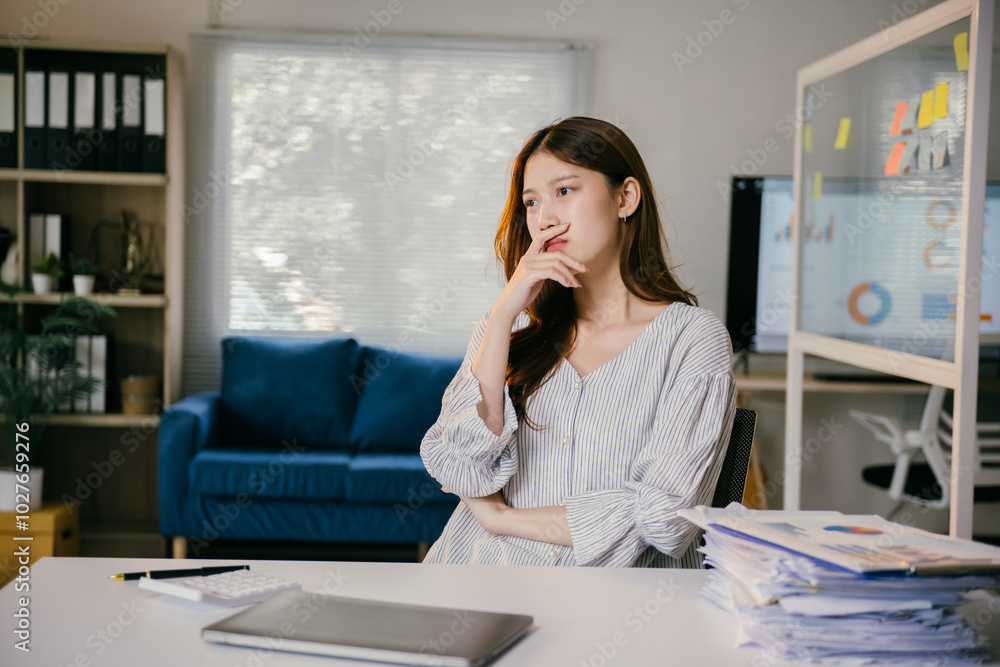 Asian businesswoman works from her home office, deep in thought, tackling a challenging problem with charts and graphs Asian businesswoman works from her home office, deep in thought, tackling a challenging problem with charts and graphs